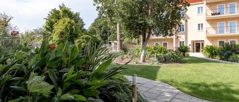 A courtyard with a paved walkway, lush greenery, and a multi-story building with balconies.