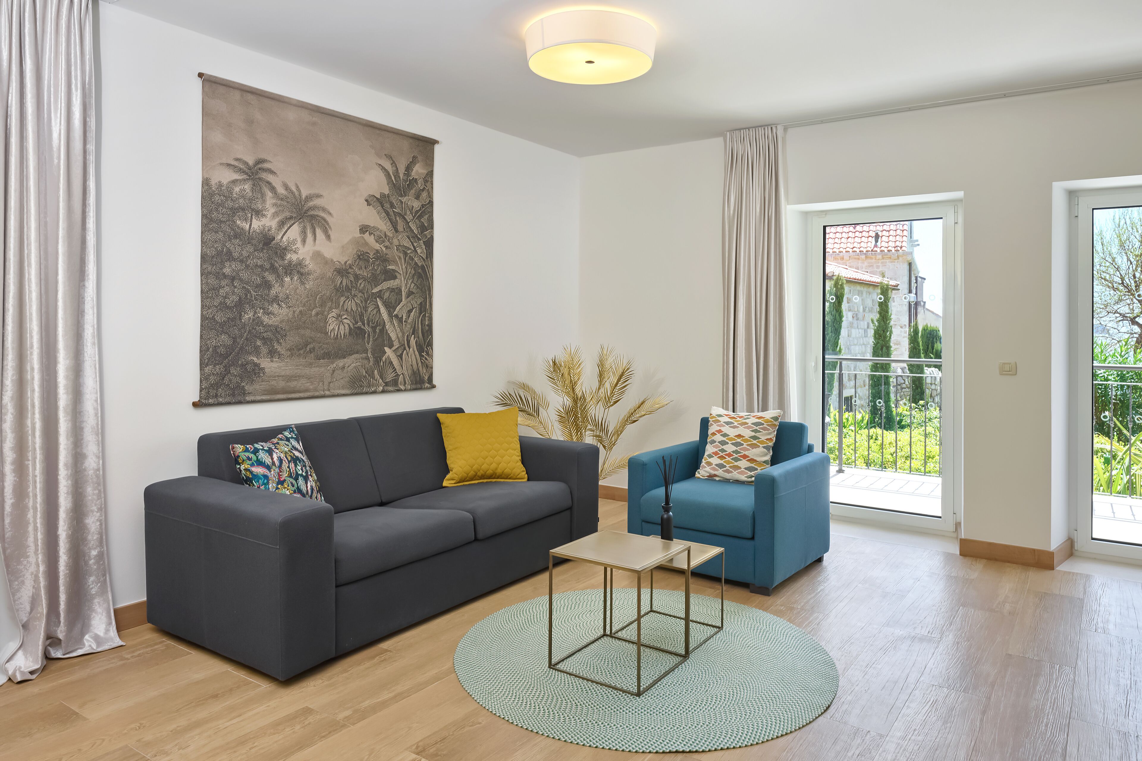 Un salon avec un canapé gris foncé, un fauteuil bleu, une petite table basse et un grand tableau accroché au mur.