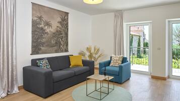 A living room with a dark grey sofa, a blue armchair, a small coffee table, and a large painting on the wall.