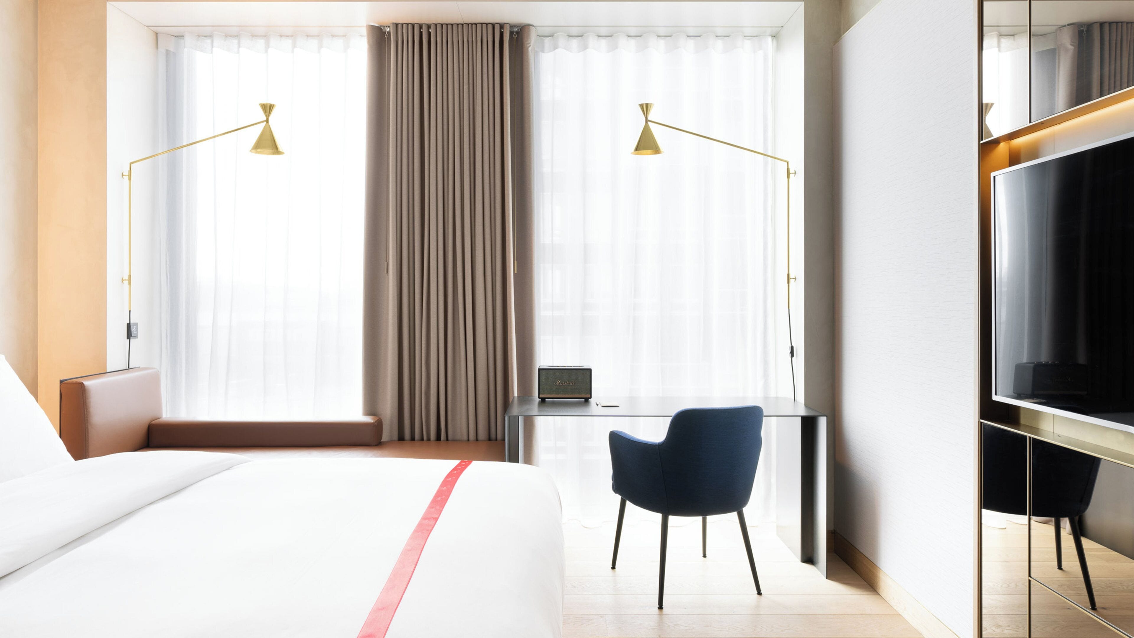A hotel room with a bed, a desk, a chair, a TV, and two lamps.