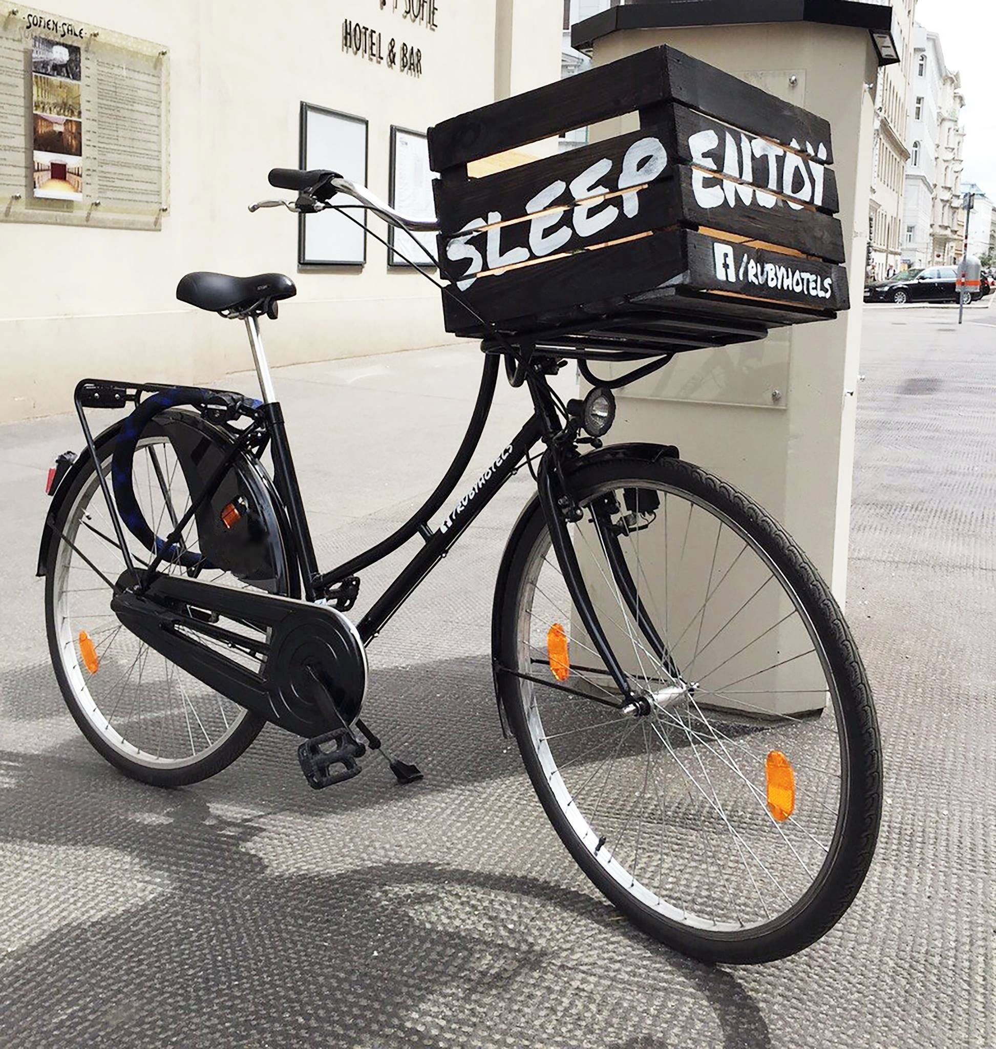 A bicycle with a delivery box labeled 'SLEEP ENJOY' parked in front of a building with a sign that reads 'HOTEL & BAR'.