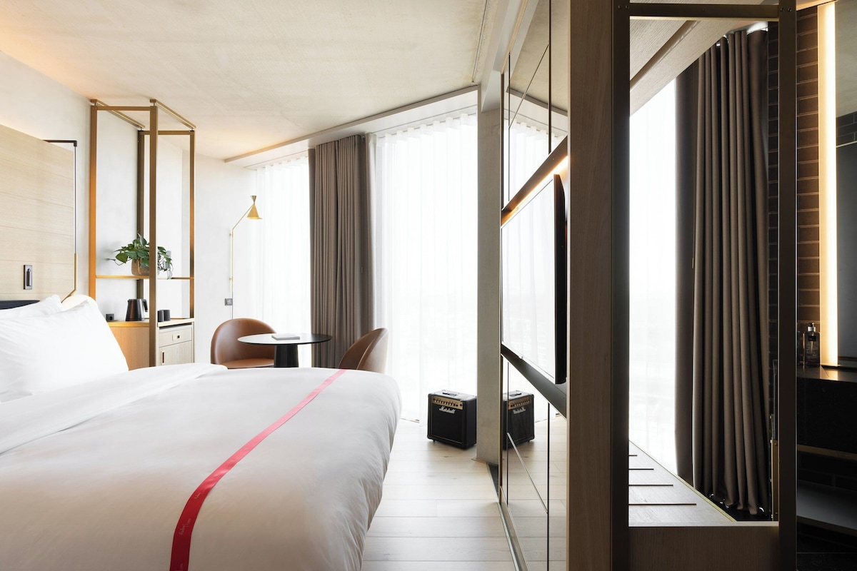 Una habitación de hotel con una cama grande, un escritorio, una silla, una planta y una ventana con cortinas.