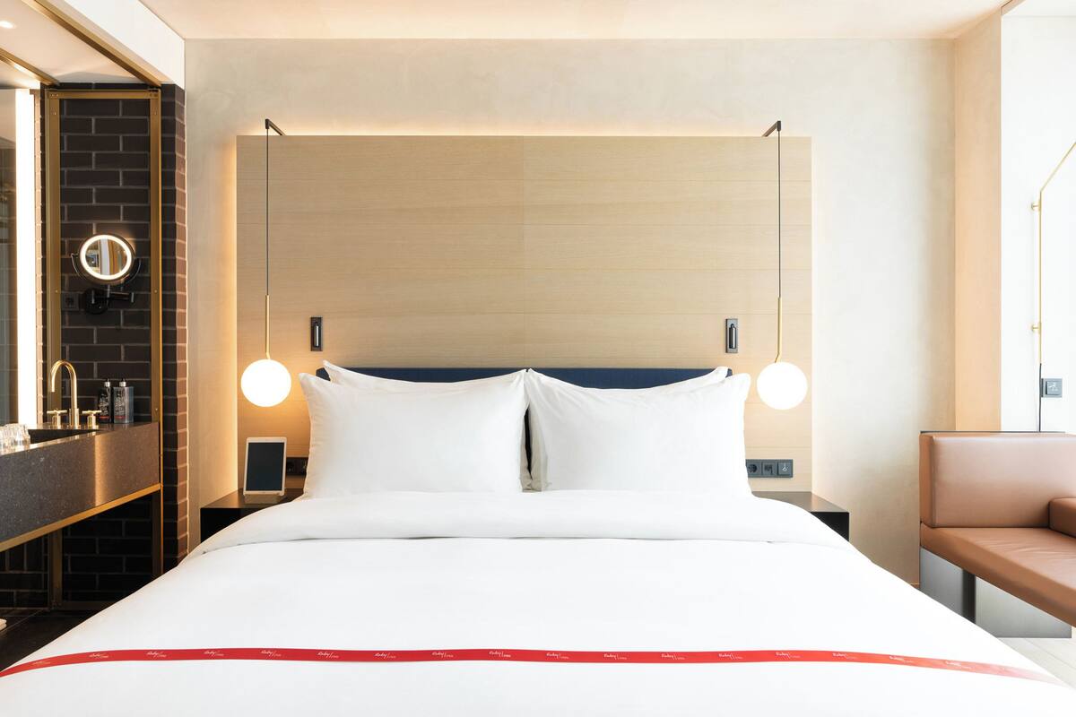 Une chambre d’hôtel comprenant un lit, des tables de chevet, un miroir, une commode, un banc et une fenêtre.