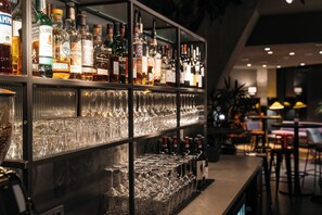 Zona de bar con estantes llenos de botellas de licor y una fila de vasos vacíos.