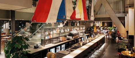 A bar area with a long counter, shelves with bottles, and a wooden barrel.