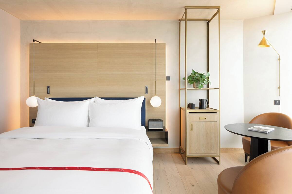 Une chambre d’hôtel comprenant un lit, une table de chevet, une lampe et un petit bureau avec une chaise.