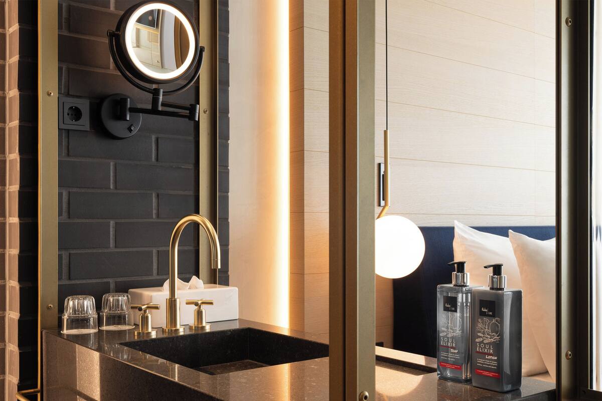 Une salle de bain moderne avec un lavabo noir, un robinet doré et un grand miroir rond doté d’un éclairage intégré.