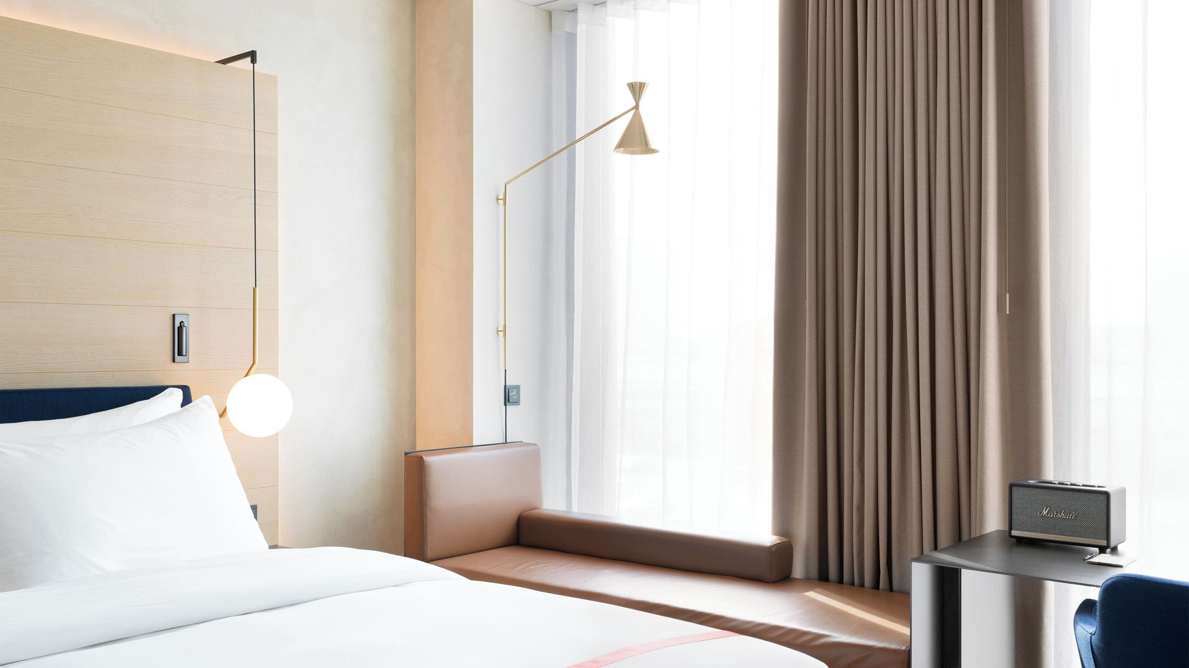 A hotel room with a bed, bedside table, lamp, and a small desk with a radio.