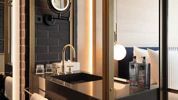 A modern bathroom with a black sink, a round mirror, and two bottles of lotion on the counter.