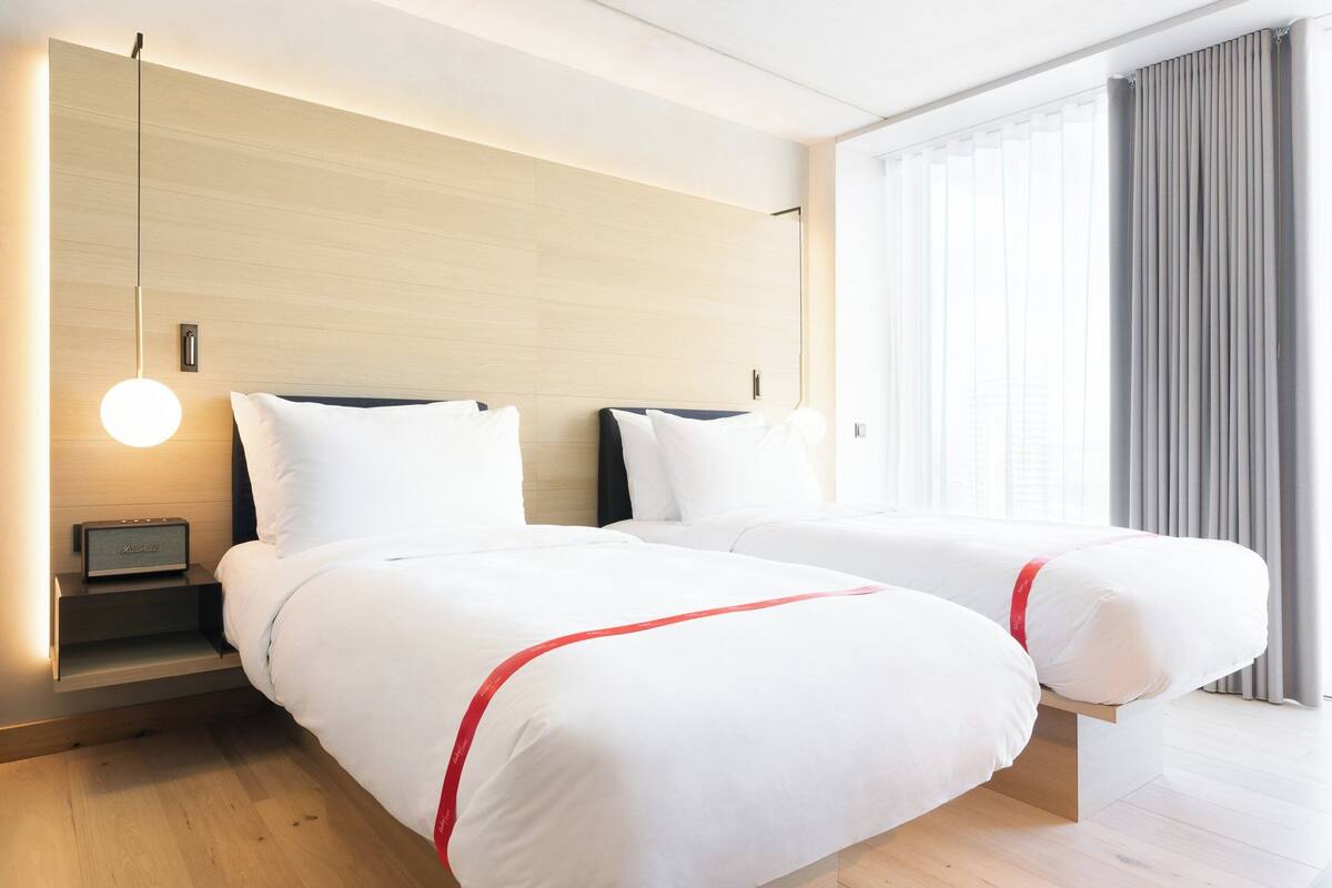 Une chambre d’hôtel avec deux lits, une table de chevet avec une lampe et une fenêtre avec des rideaux.