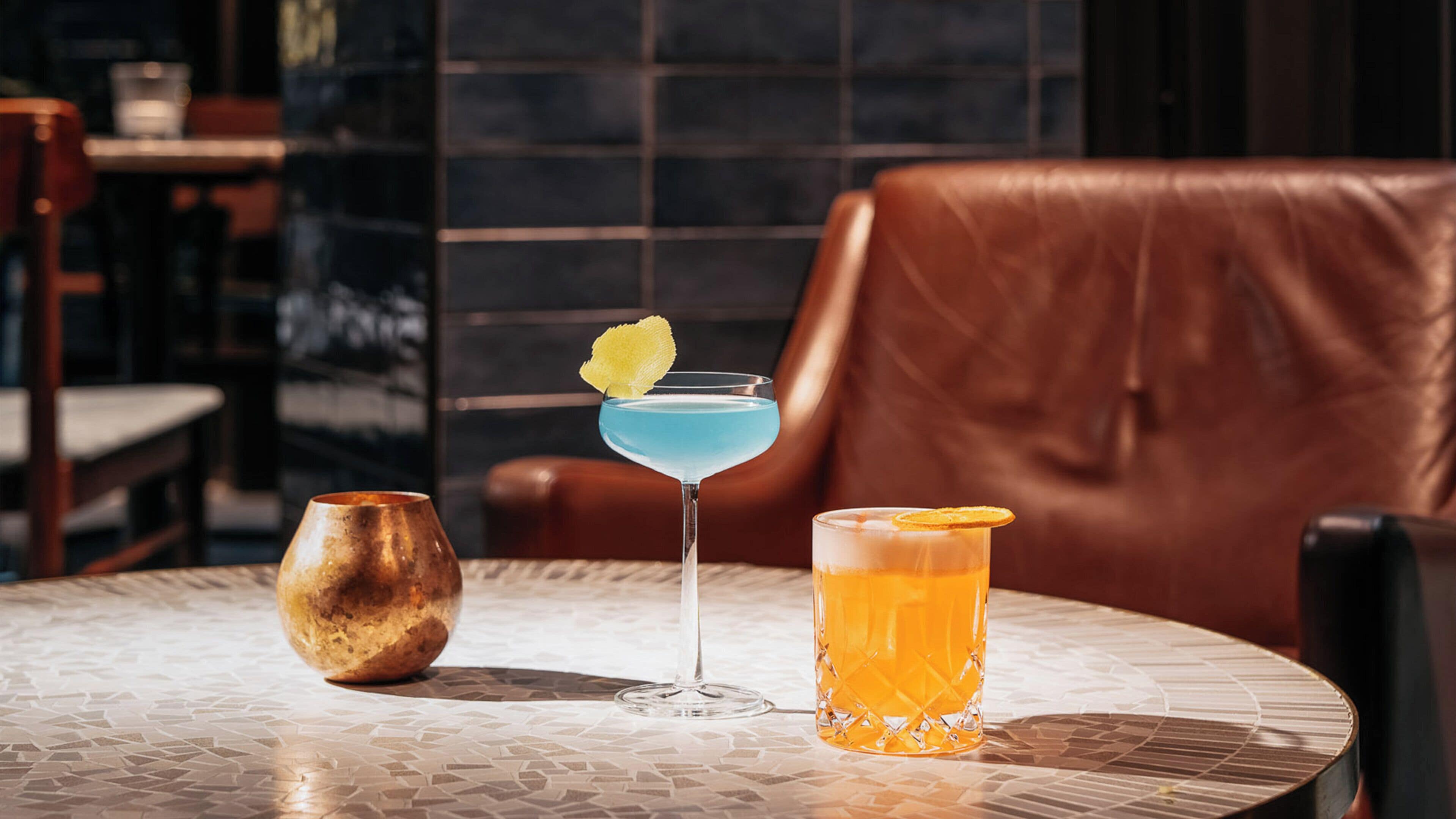A round table with two drinks, a decorative bowl, and a leather chair.