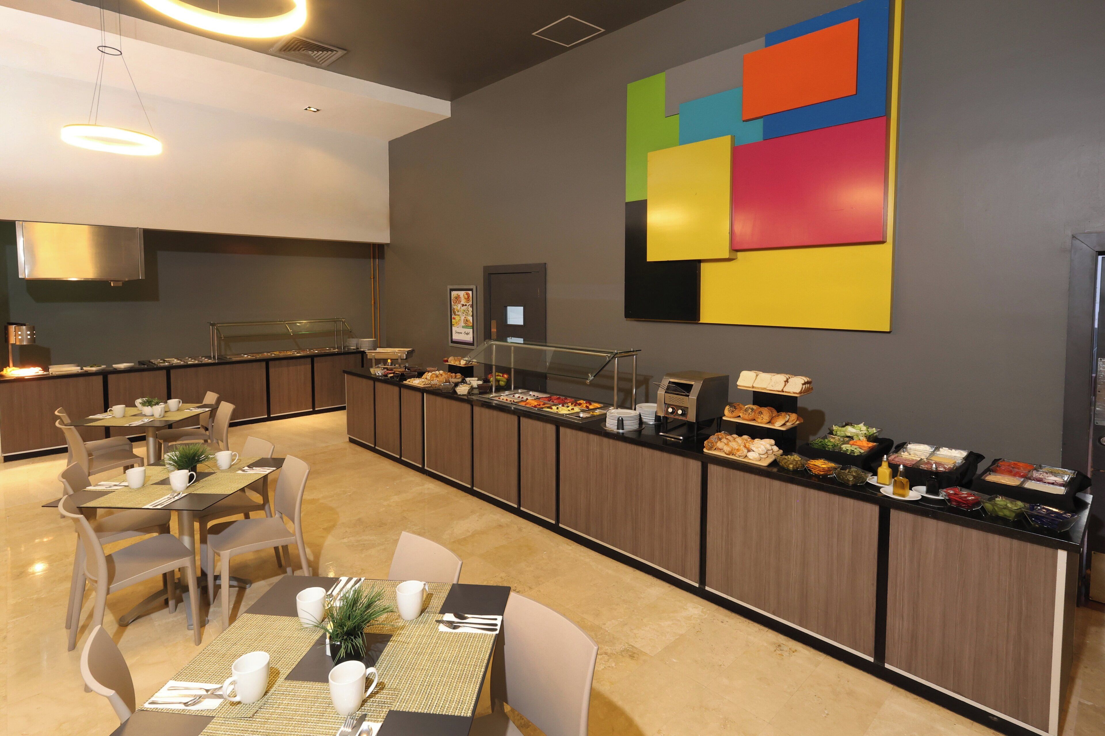 A modern hotel dining area with a buffet, multiple dining tables, and chairs.