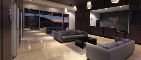 A modern hotel lobby with a large seating area, a reception desk, and a large window offering a view of the cityscape.