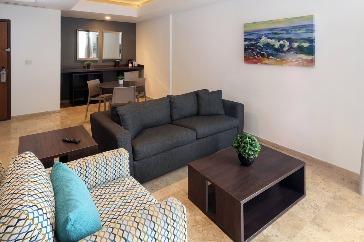 A living room with a grey sofa, patterned sofa, and a coffee table with a plant.