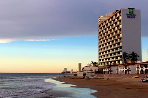 Un hotel frente a la playa con un edificio grande, una playa de arena y el océano.