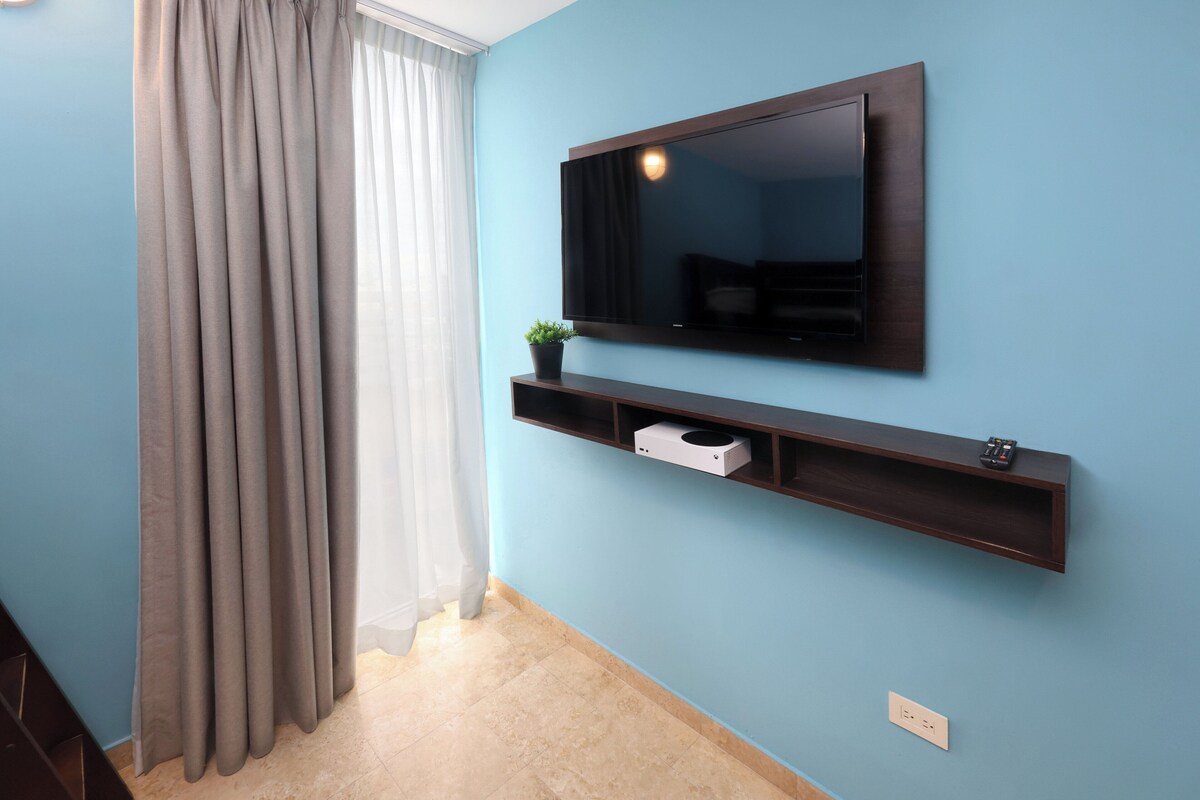 Quarto com televisão montada, prateleira com planta e interruptor de luz na parede.
