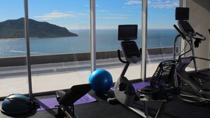 Un gimnàs amb equipament esportiu i una gran finestra amb vista a un cos d'aigua i una illa a la distància.