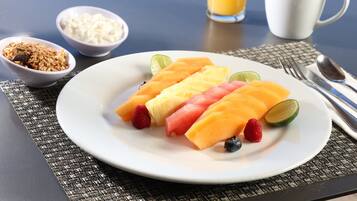 En una mesa, un plato de ensalada de frutas, un vaso de jugo de naranja y recipientes con yogur y granola.