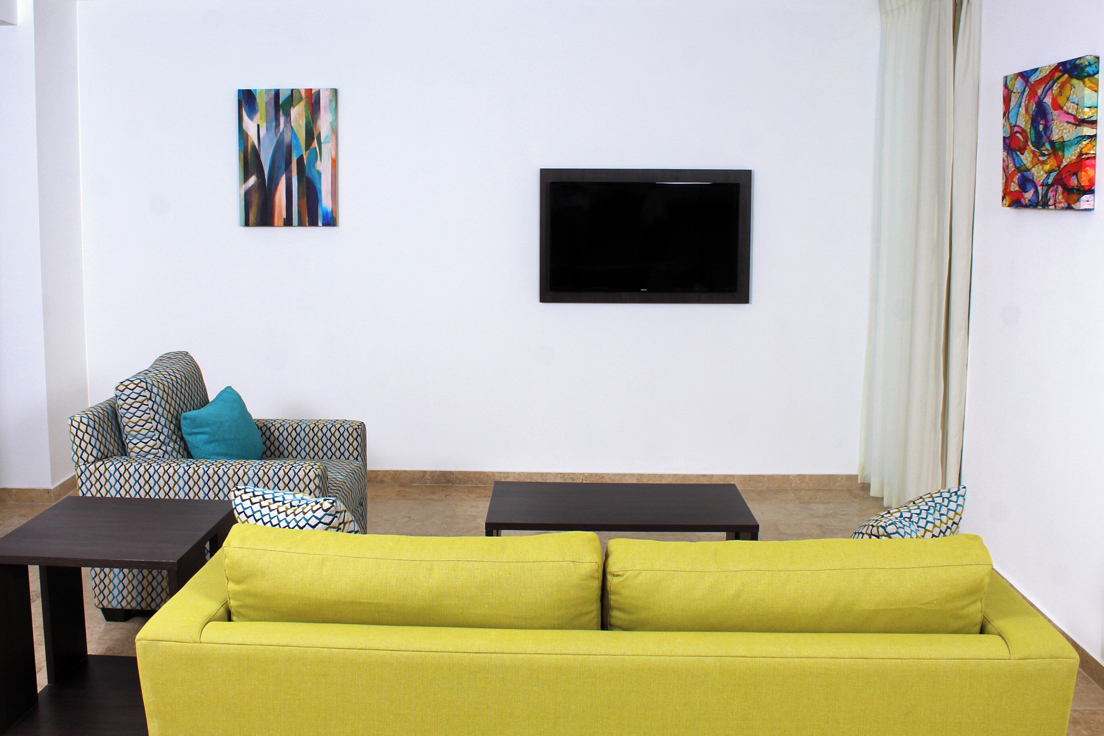 A living room with a sofa, a patterned armchair, a coffee table, and a flat-screen TV mounted on the wall.