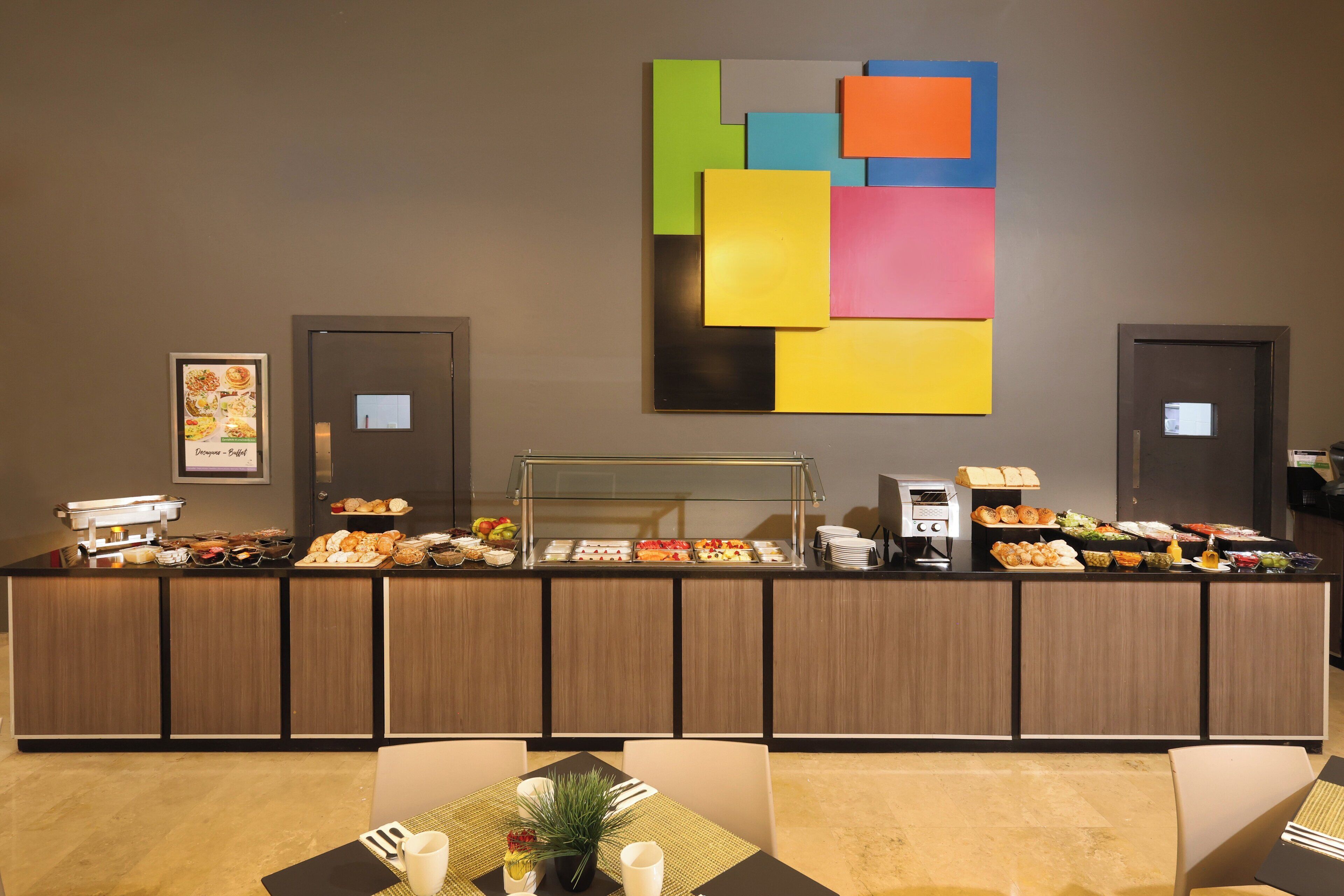 A buffet area with a variety of food items, a coffee machine, and a colorful abstract painting on the wall.