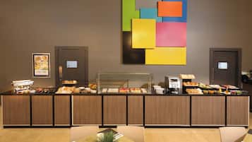 A buffet area with a variety of food items, a coffee machine, and a colorful abstract painting on the wall.