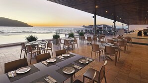 A restaurant with outdoor seating overlooking the sea, featuring tables with place settings and chairs.