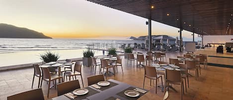 A restaurant with outdoor seating overlooking the sea, featuring tables with place settings and chairs.