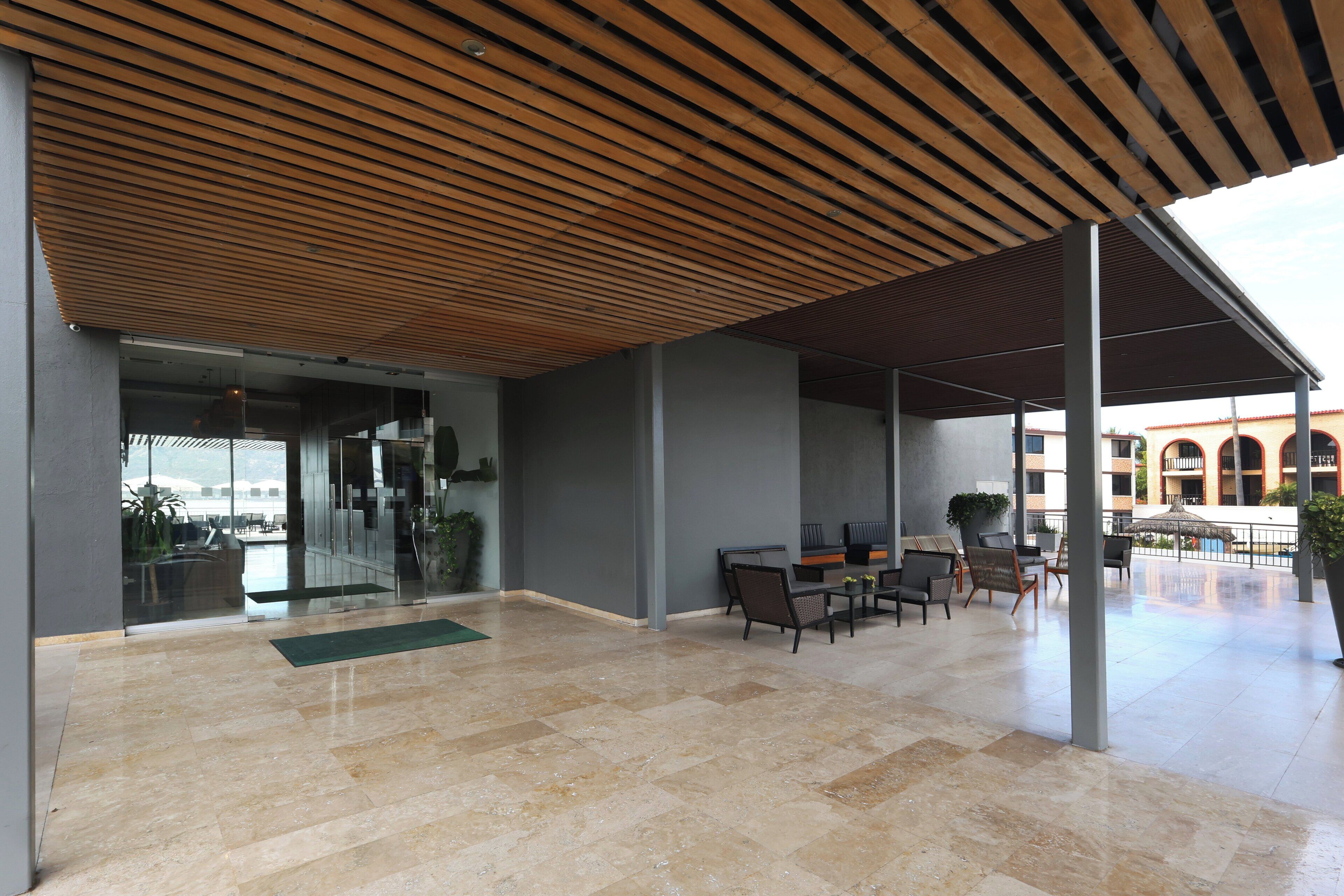 Un vaste espace intérieur doté d’un plafond en bois, de différents espaces aménagés pour s’asseoir et d’une vue sur un bâtiment orné d’arcades.