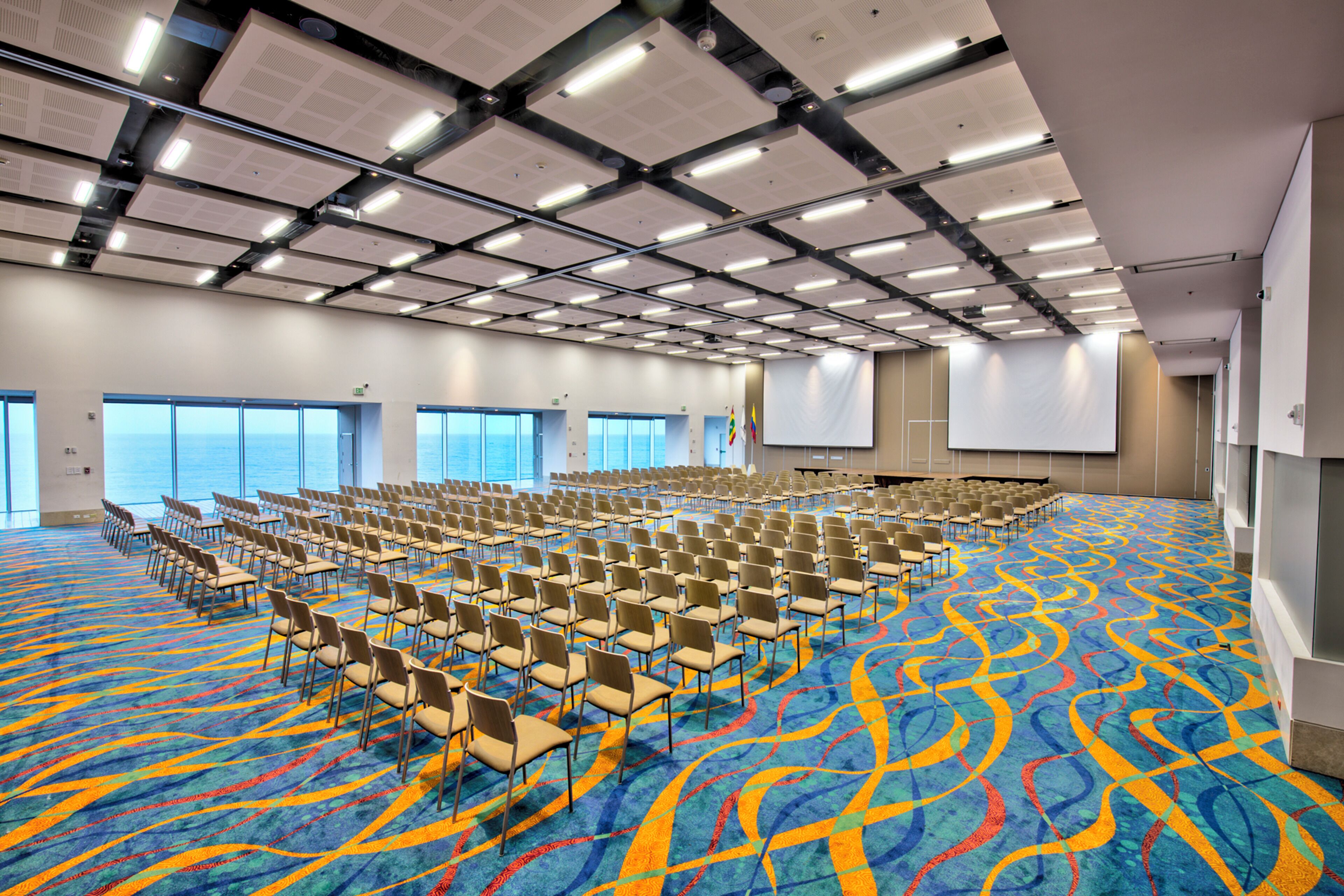 A large conference room with rows of chairs, a colorful carpet, and a projector screen.