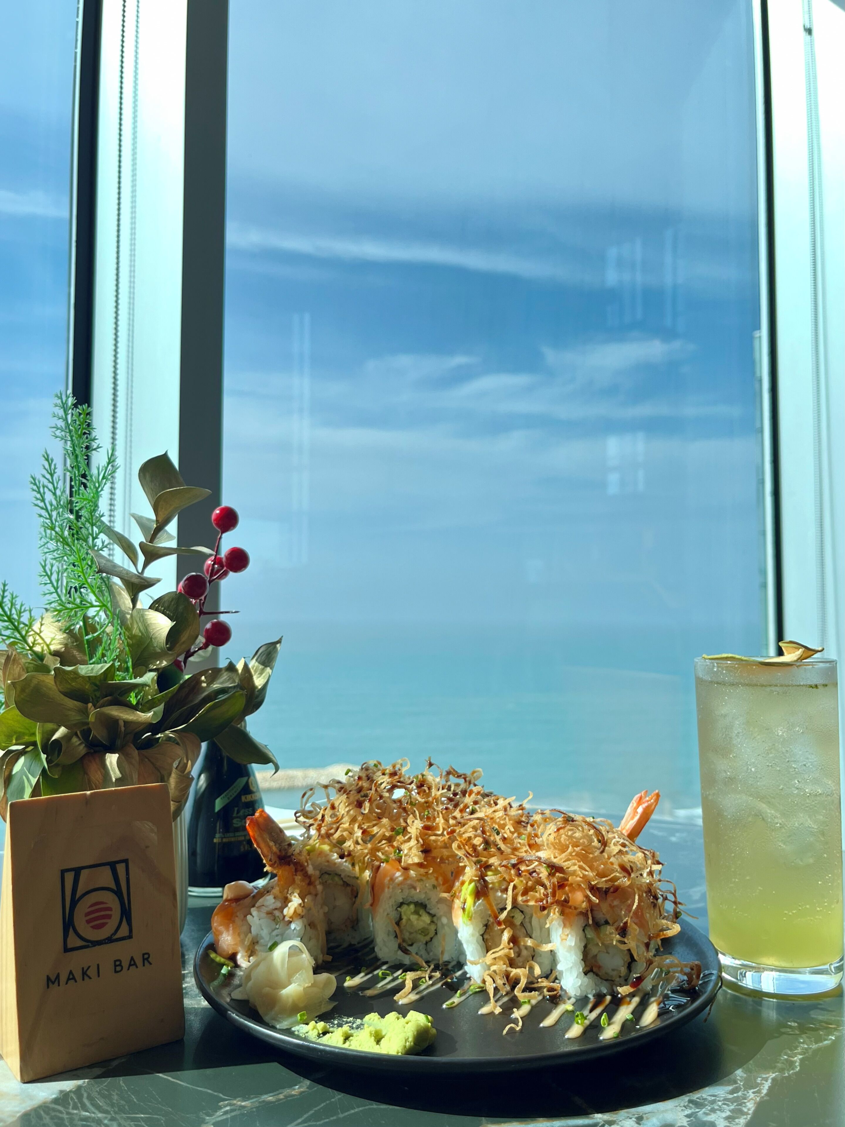 A sushi platter with a drink and a plant on a table by a window.