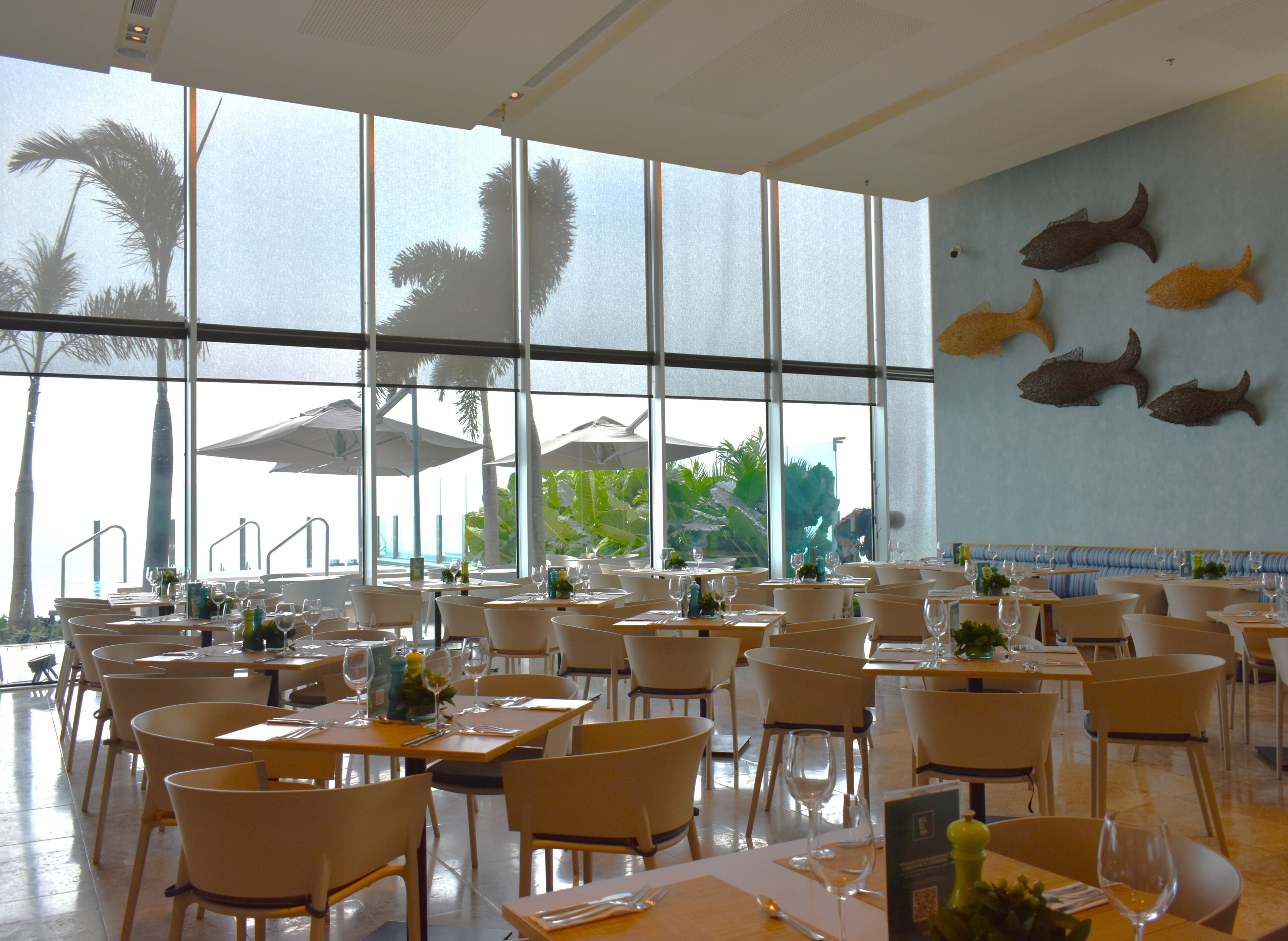 A spacious restaurant with large windows, white chairs, and tables set for dining.