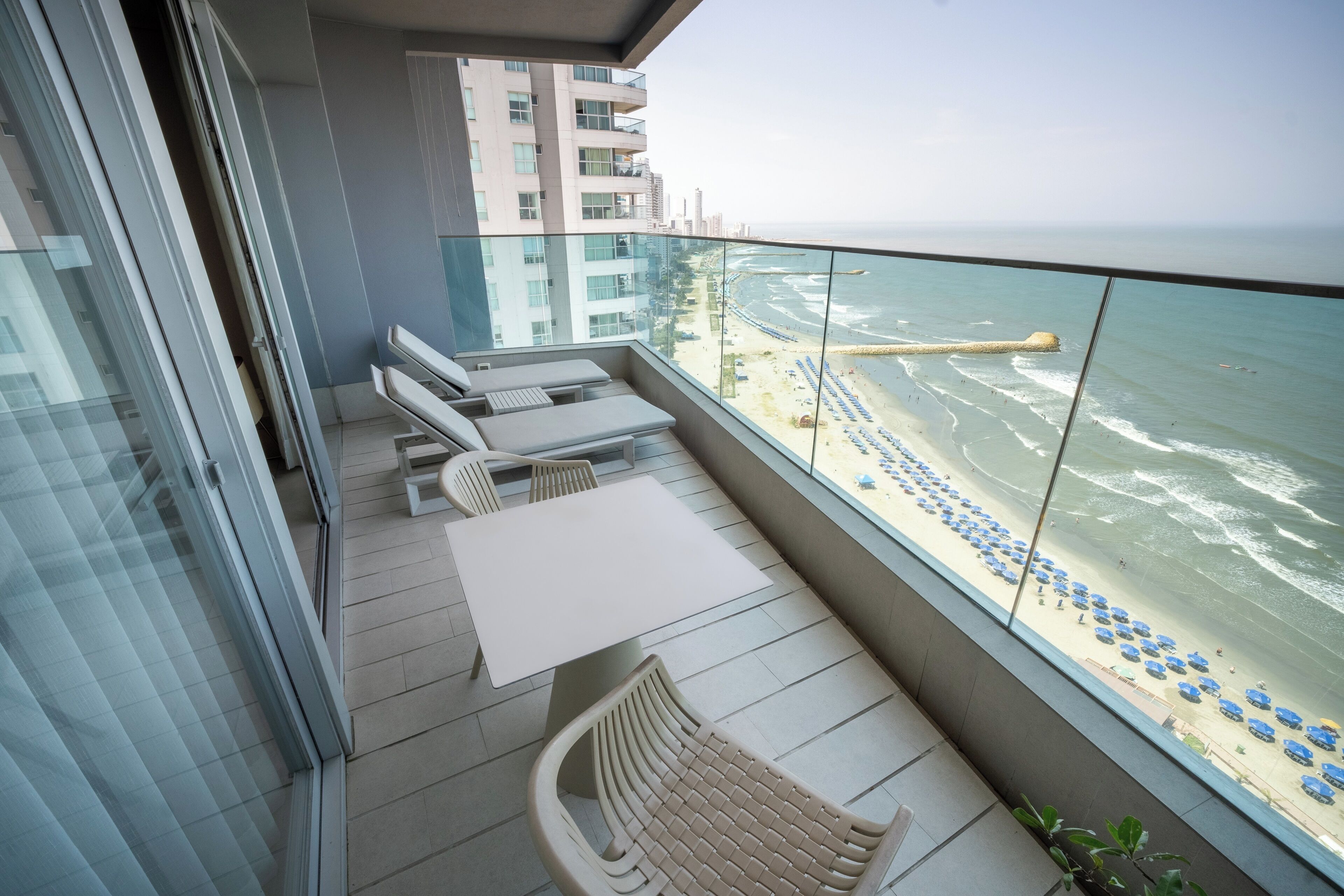 A balcony with a view of the beach, a table, and two chairs.