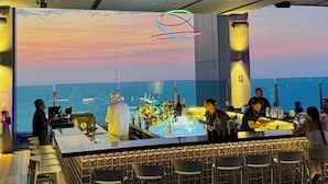 A bar area with a view of the sea, bar stools, and a bartender.