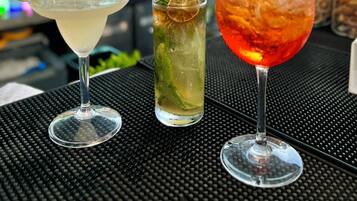 Three cocktails on a bar counter with a bartender in the background.