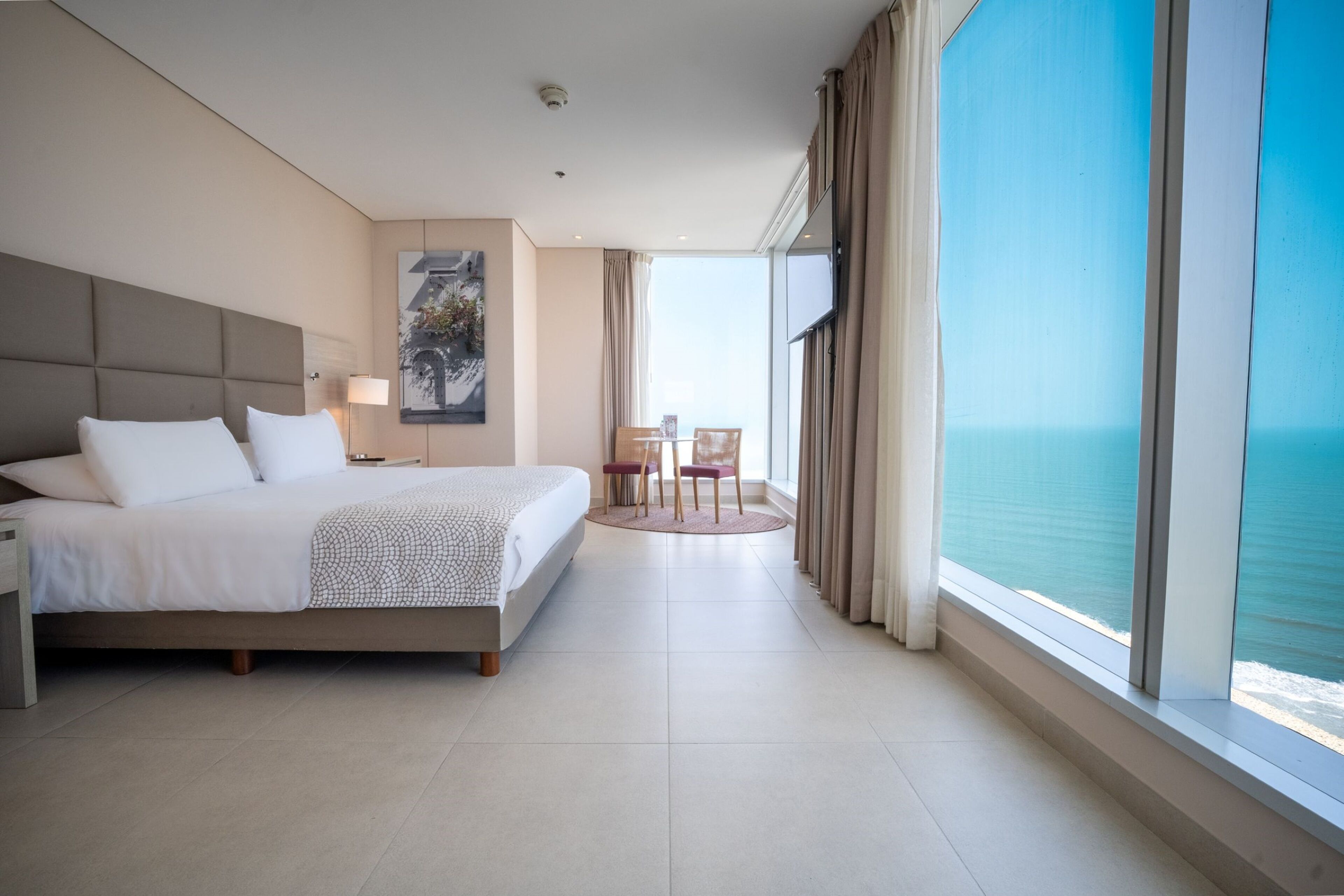 Habitación de hotel con una cama grande, un escritorio, una silla, una mesa y vistas al océano.