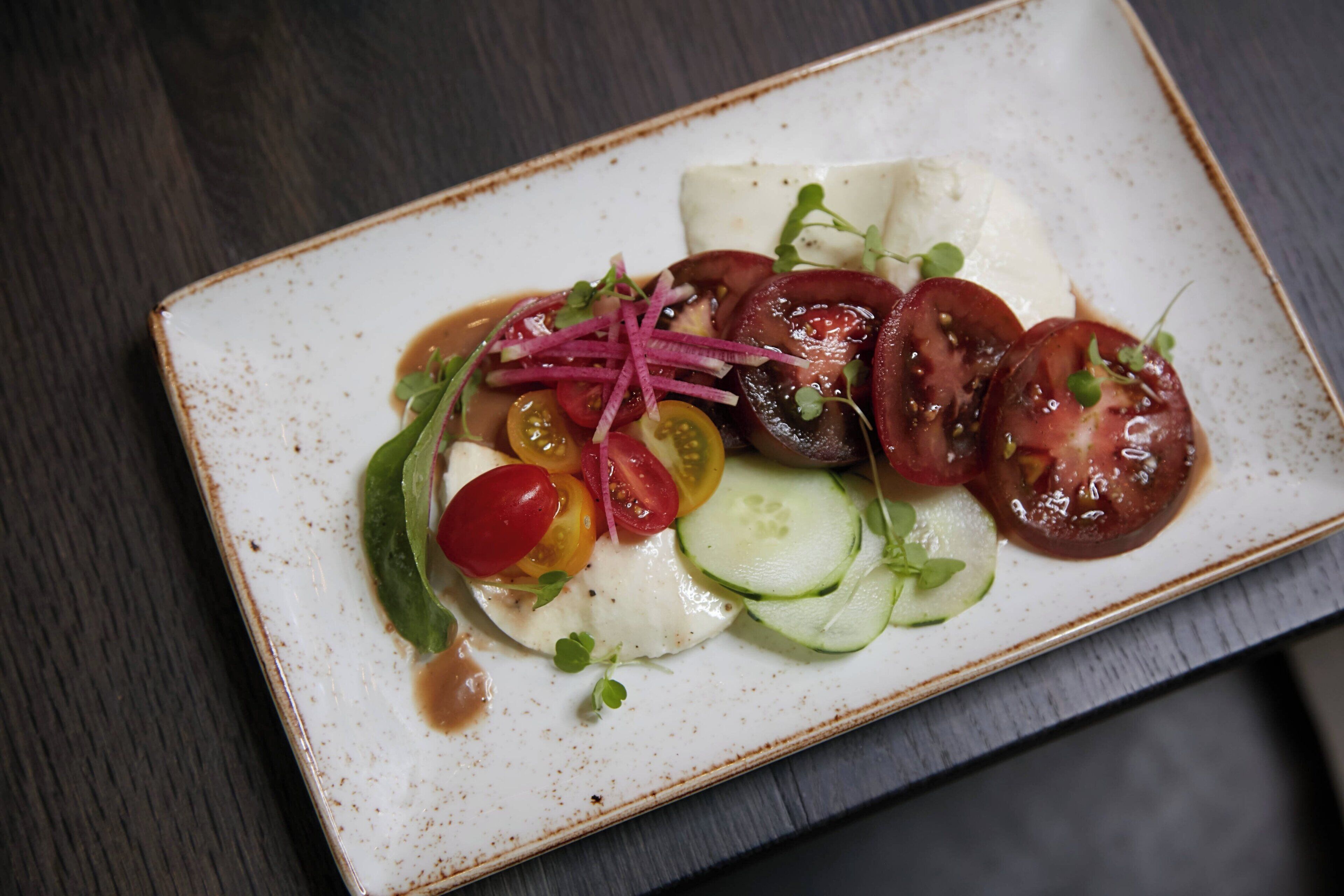 A rectangular plate with a white base and a brown rim, containing a salad with various vegetables and a white sauce.