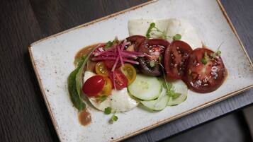 A rectangular plate with a white base and a brown rim, containing a salad with various vegetables and a white sauce.