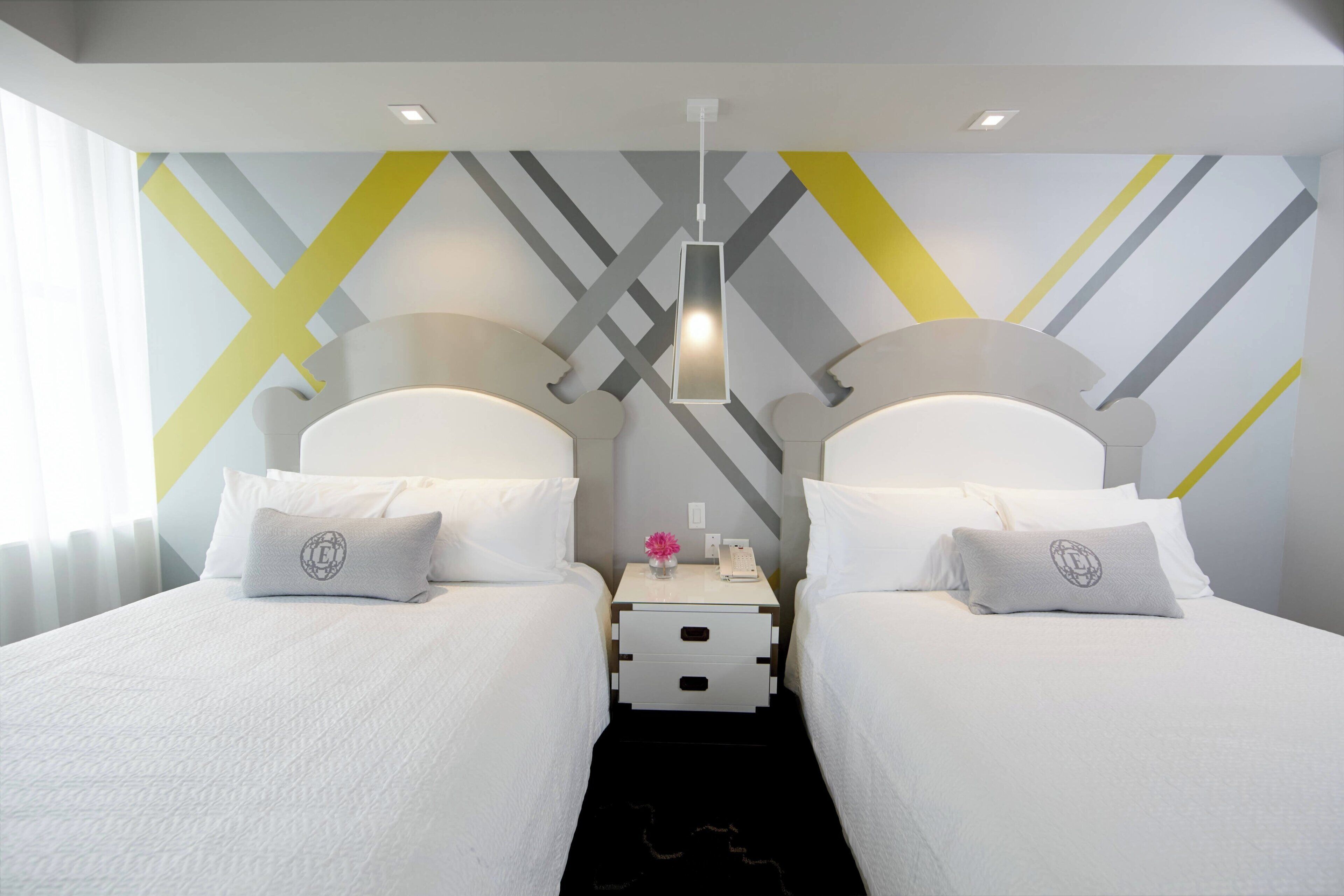 A hotel room with two beds, a nightstand, a lamp, and a geometric-patterned wall.