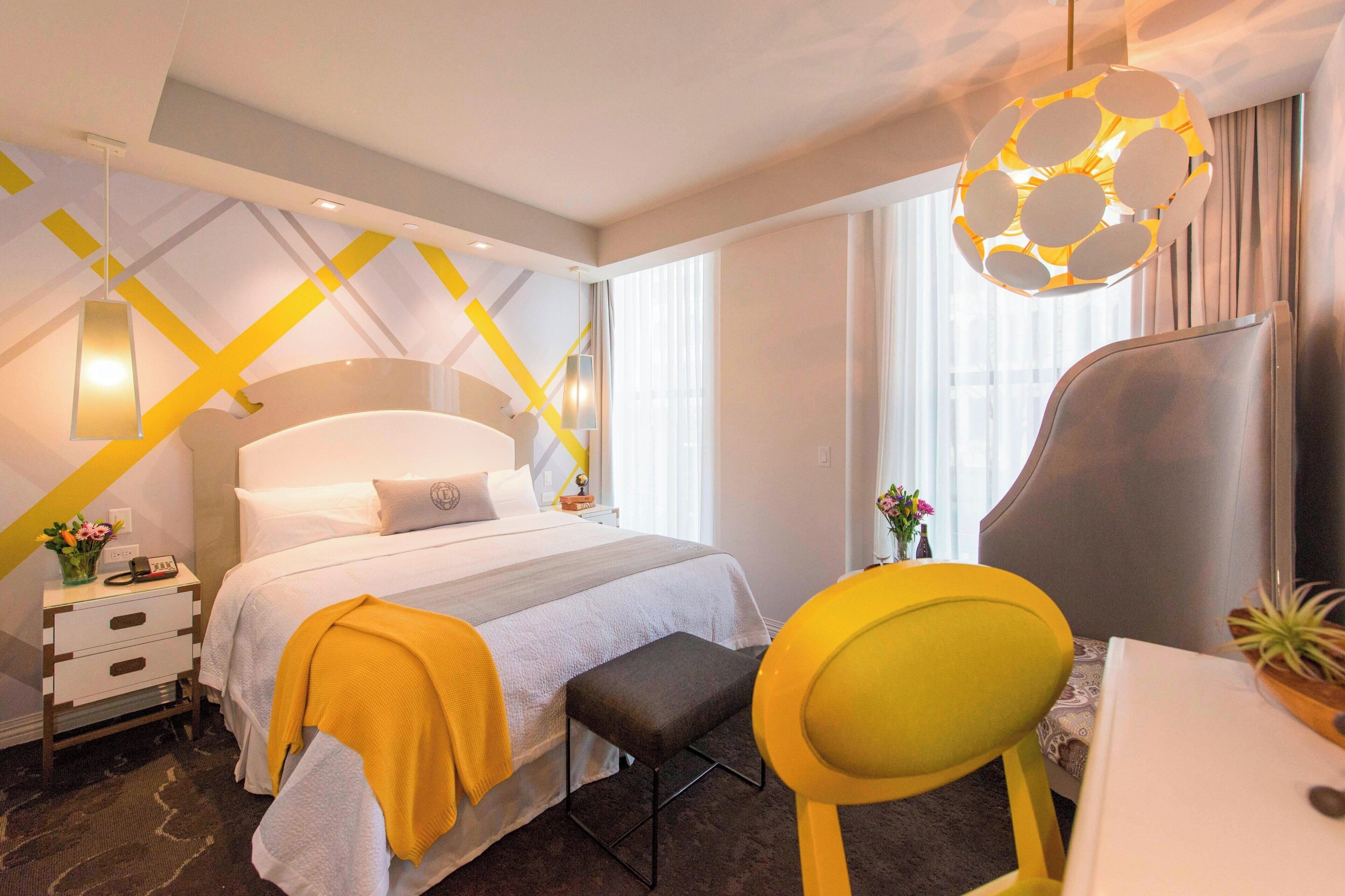 Ein Hotelzimmer mit Bett, Nachttisch, Stuhl, Schreibtisch und einer Pendelleuchte.