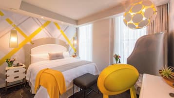Ein Hotelzimmer mit Bett, Nachttisch, Stuhl, Schreibtisch und einer Pendelleuchte.