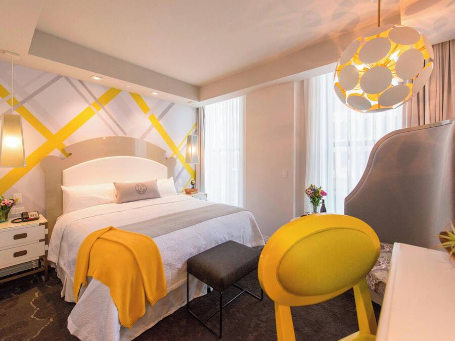 Ein Hotelzimmer mit Bett, Nachttisch, Stuhl, Schreibtisch und einer Pendelleuchte.