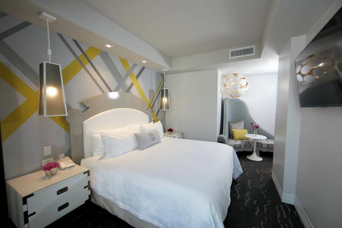 Ein modernes Hotelzimmer mit einem großen Bett, Nachttischen, einem Schreibtisch und einem Fernseher.