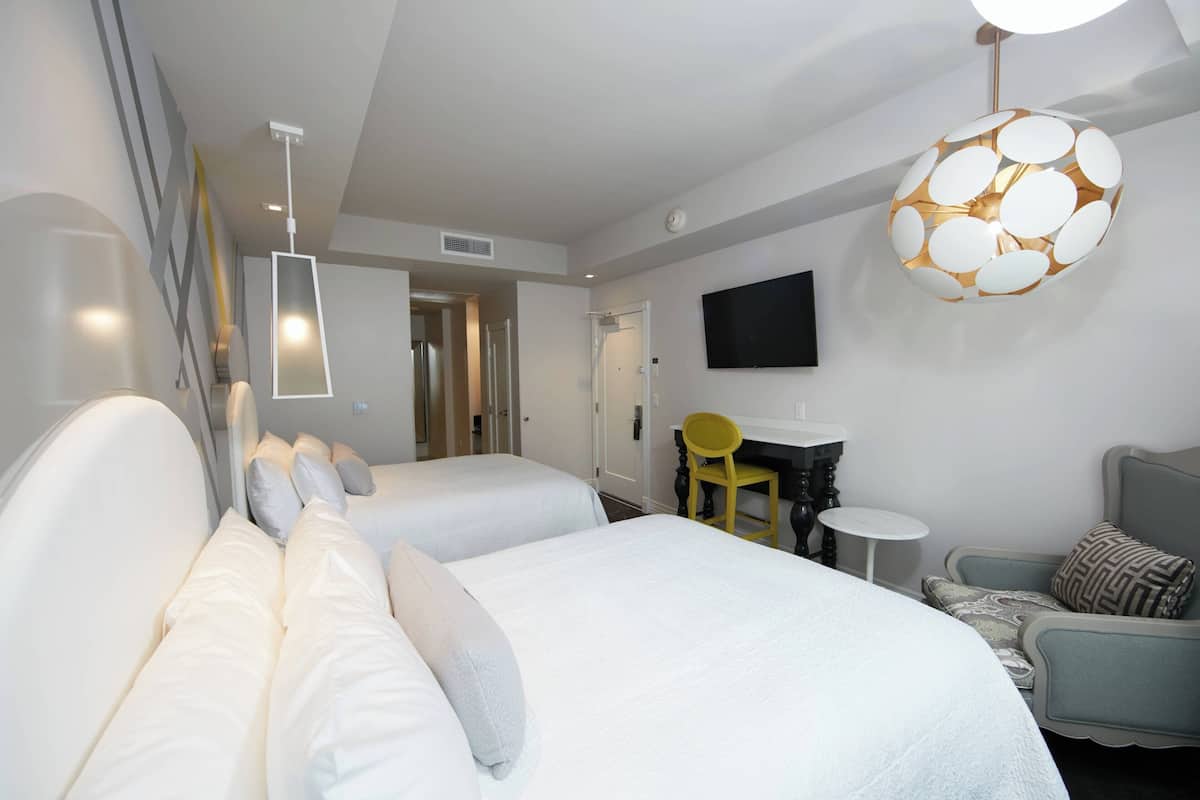 Ein Hotelzimmer mit zwei Betten, einem Schreibtisch mit Stuhl, einem kleinen runden Tisch, einem an der Wand montierten Fernseher und einer ungewöhnlichen, kugelförmigen Lampe.