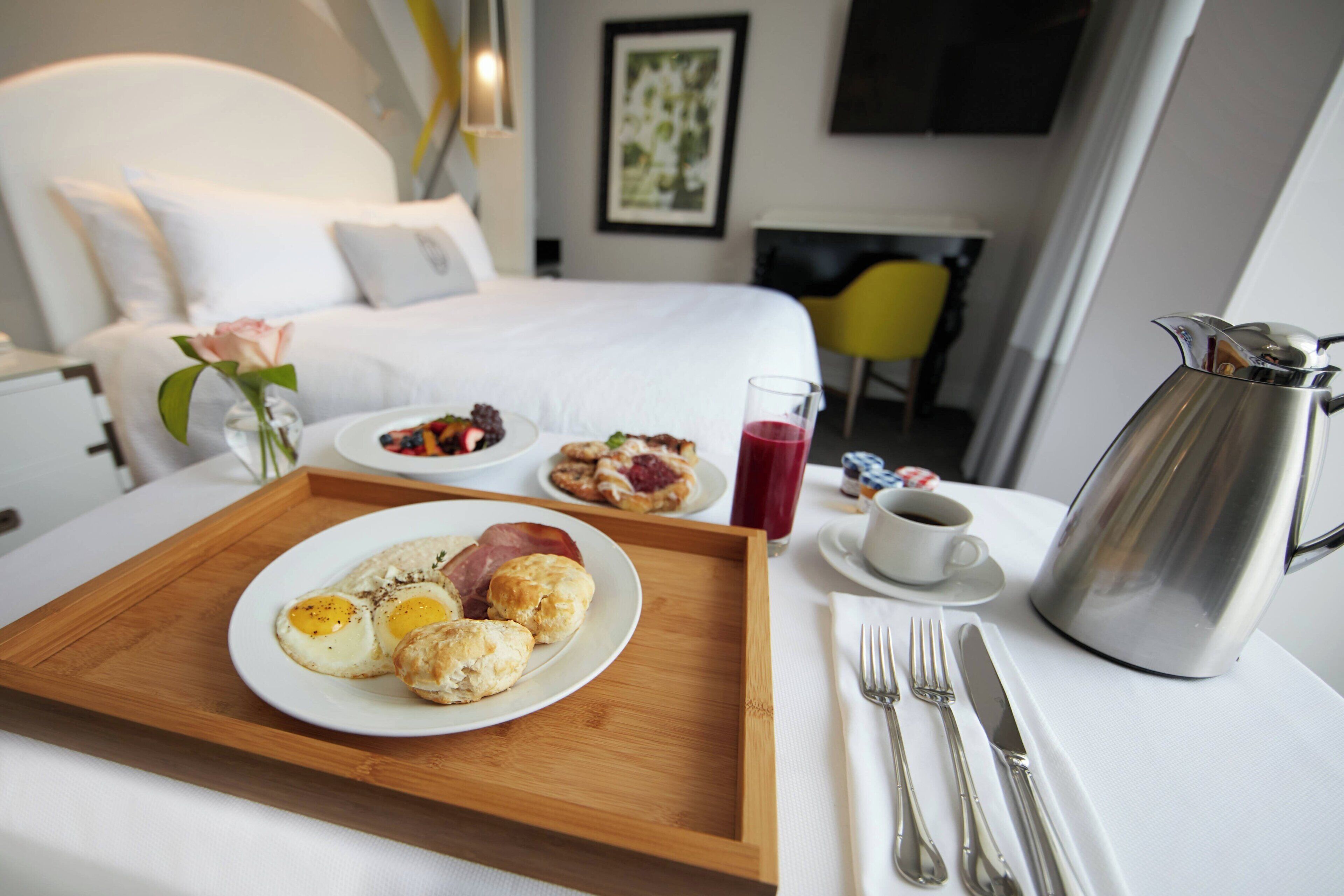 A hotel room with a bed, a breakfast tray with eggs, pastries, and a coffee pot.
