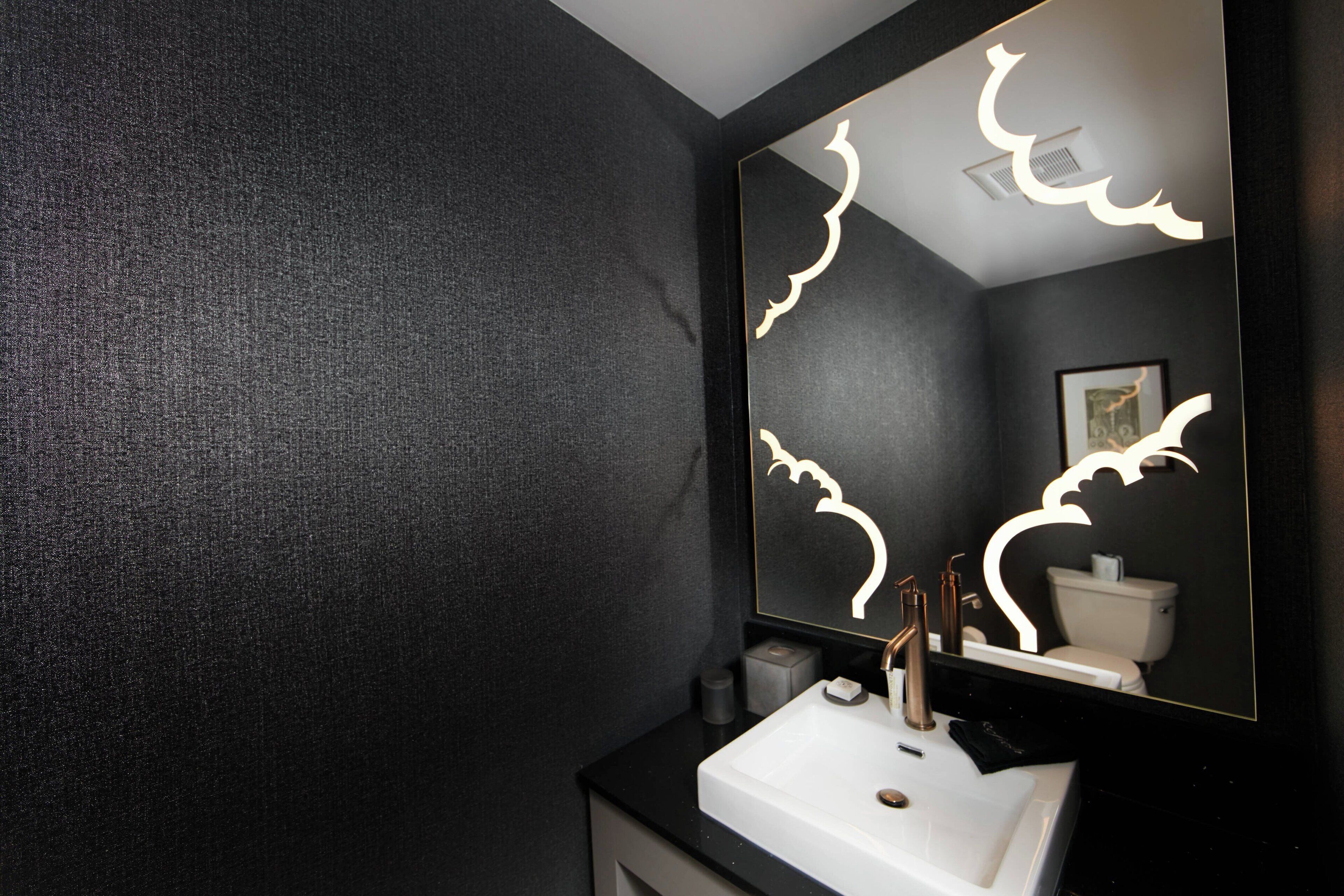 A bathroom with a dark textured wall, a white sink, and a mirror with light patterns.