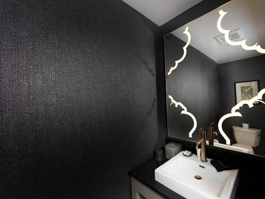 A bathroom with a dark textured wall, a white sink, and a mirror with light patterns.