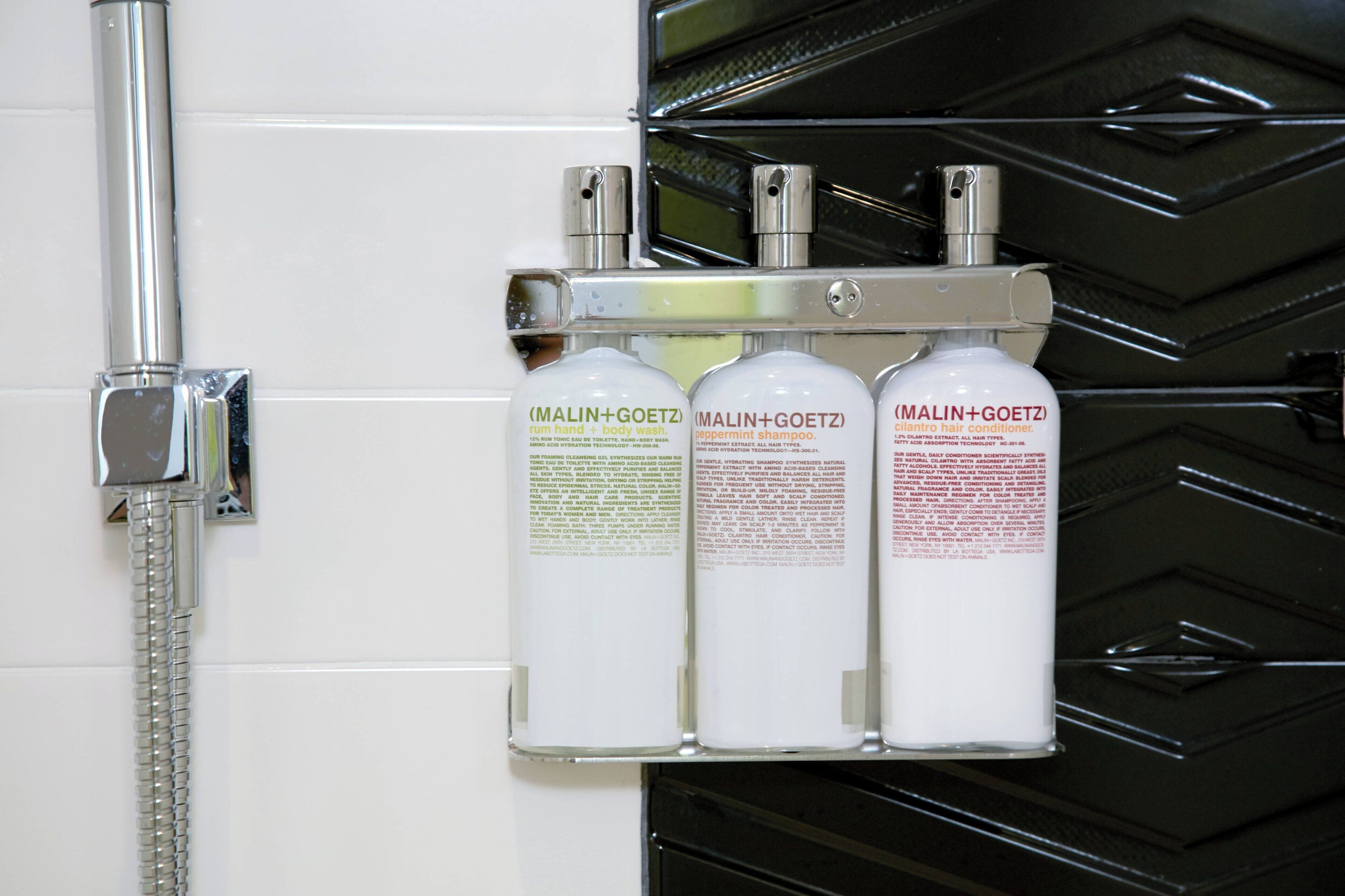 Un espace douche équipé d’un robinet chromé et de trois flacons de gel douche de la marque MALIN+GOETZ.