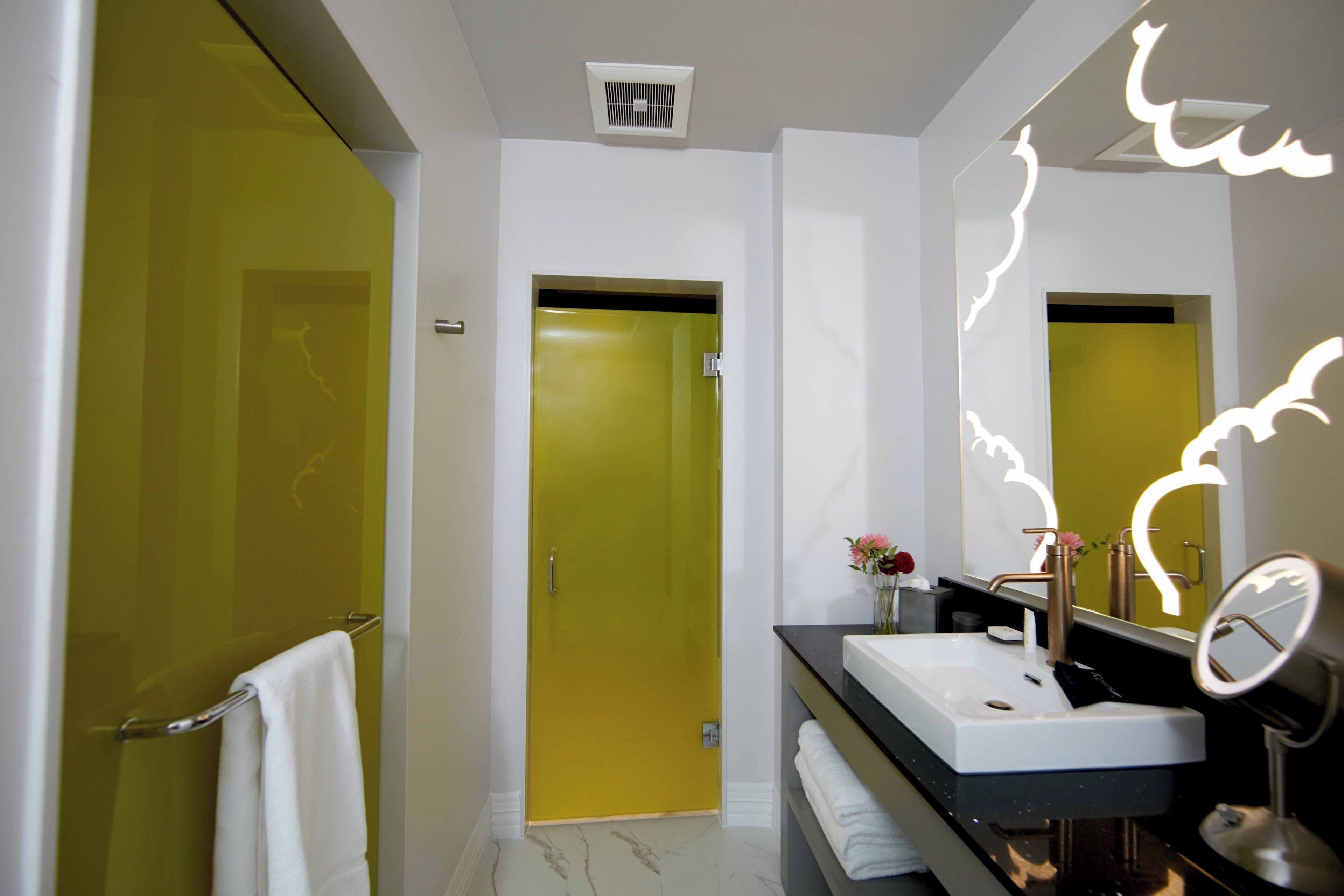 A modern bathroom with a yellow door, a white sink, and a mirror.
