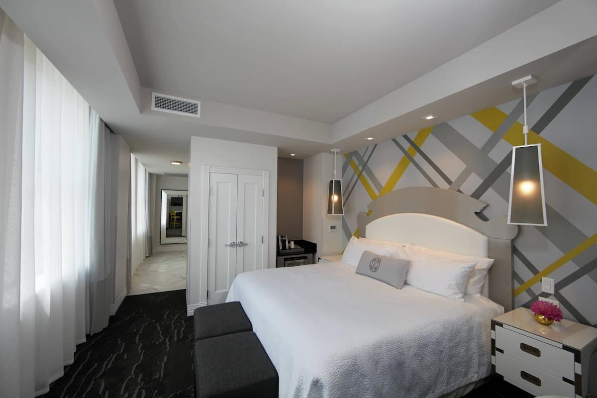 Ein Hotelzimmer mit Bett, Nachttisch, Lampe und Blick auf den Flur.
