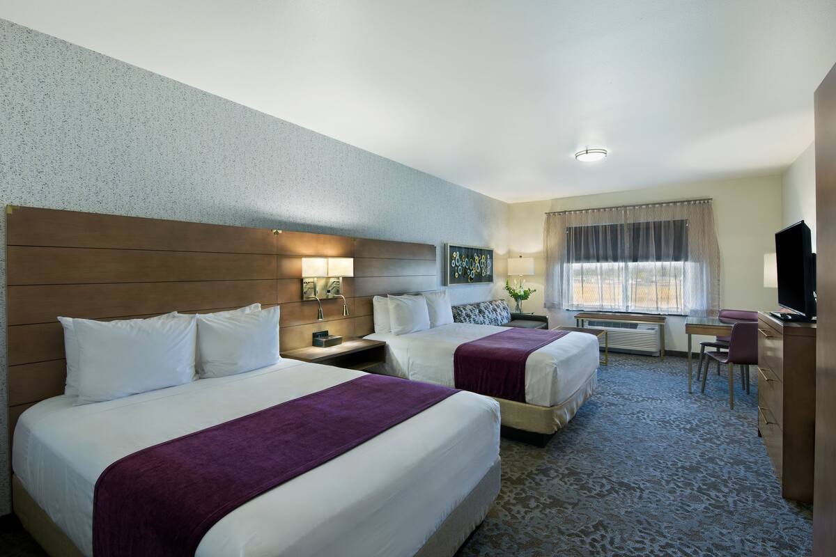 Ein Hotelzimmer mit zwei Betten, einem Schreibtisch, einem Stuhl, einem Fernseher und einem Fenster mit Vorhängen.